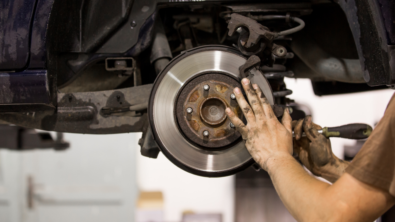 A man is fixing a brake disc on a car in a garage.