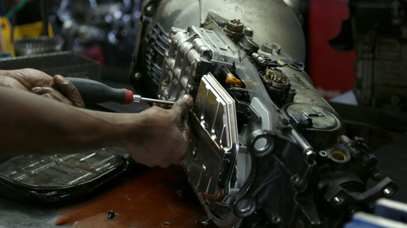 A man is working on a car engine with a screwdriver.