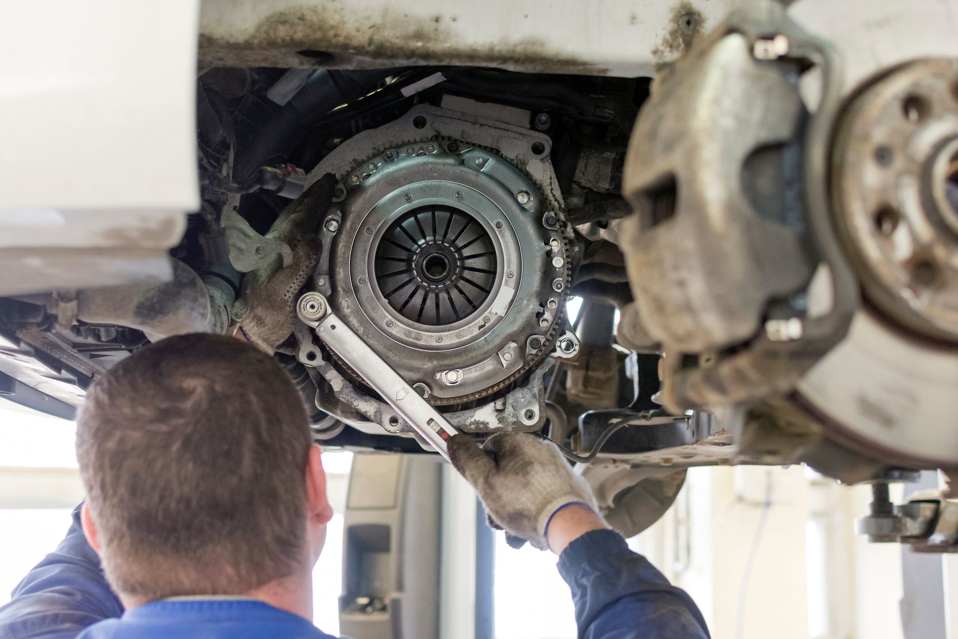 Mechanic working under a car, inspecting the exposed clutch assembly with a wrench