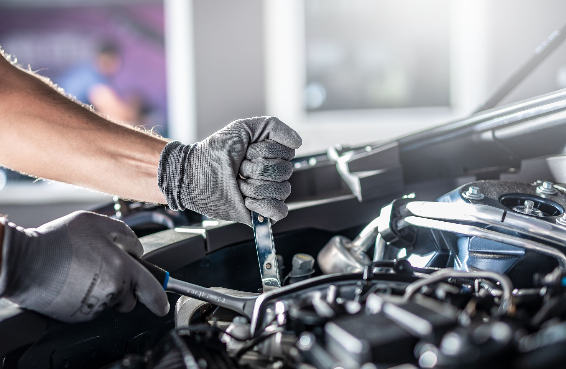 Mechanic wearing gloves working under a car hood in a garage