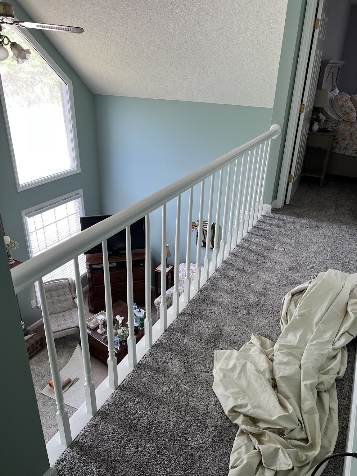 Overhead view of a white railing on a carpeted second floor overlooking a living room with a TV and blue walls.
