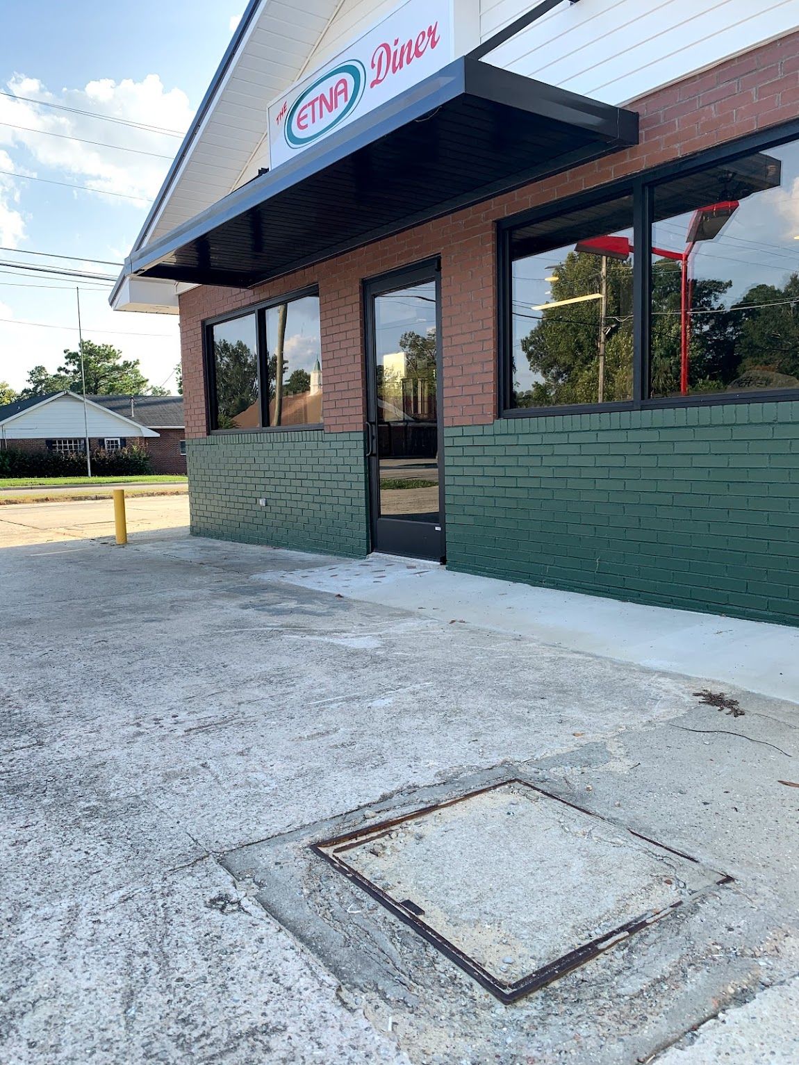 Exterior of a diner with black awning, windows, and brick facade. Green painted brick base and concrete ground.