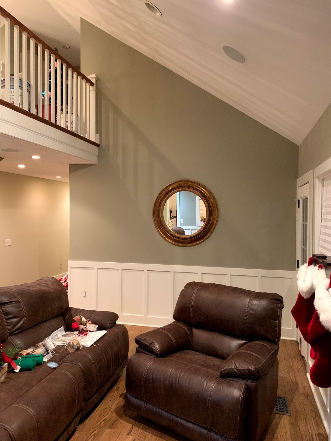 Living room with leather recliners, a gold-framed mirror on a sage green wall, and a staircase.