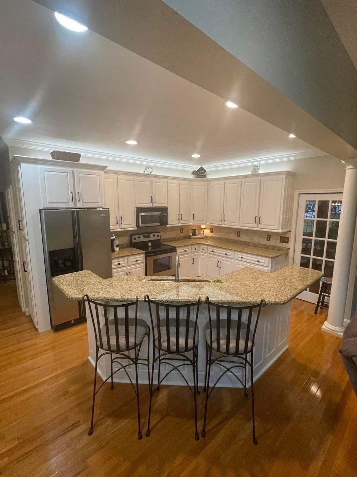 Kitchen with white cabinets, granite countertops, island with three stools, and hardwood floors.