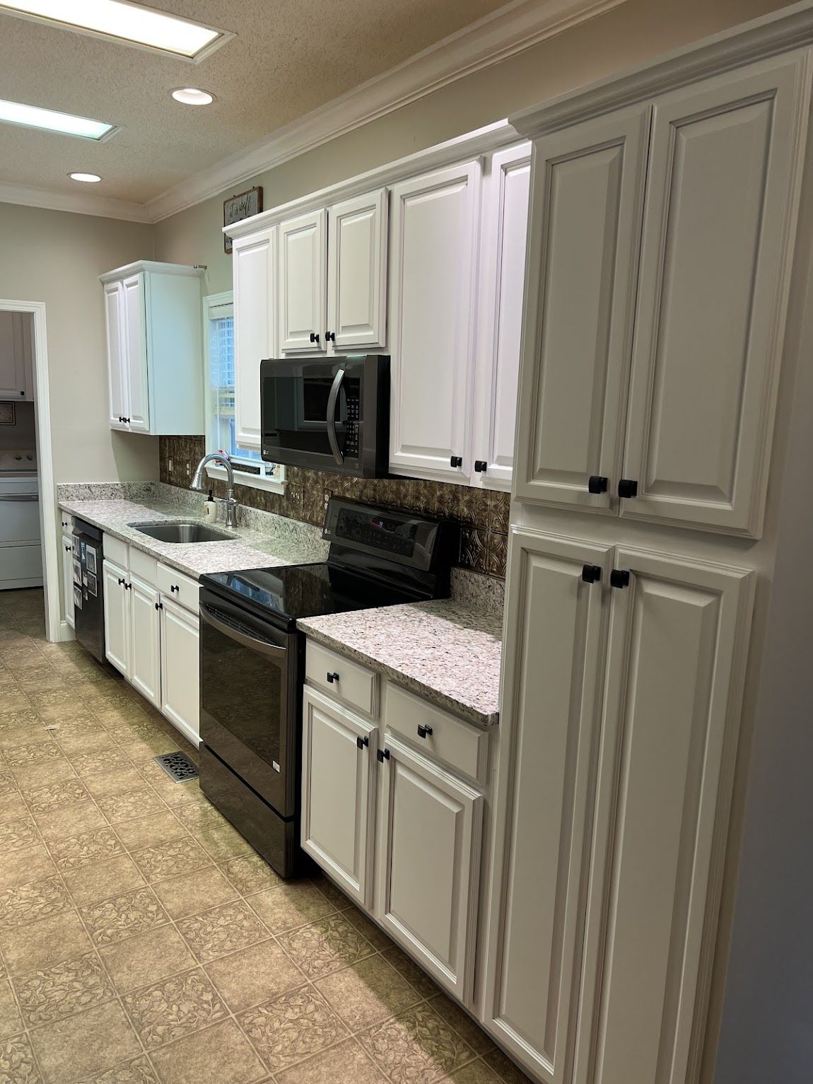 White kitchen cabinets with black appliances and speckled countertops.