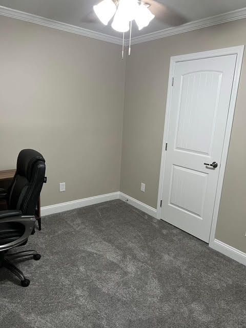 Empty home office with gray walls, white door, and gray carpet. A desk with a black chair is visible.