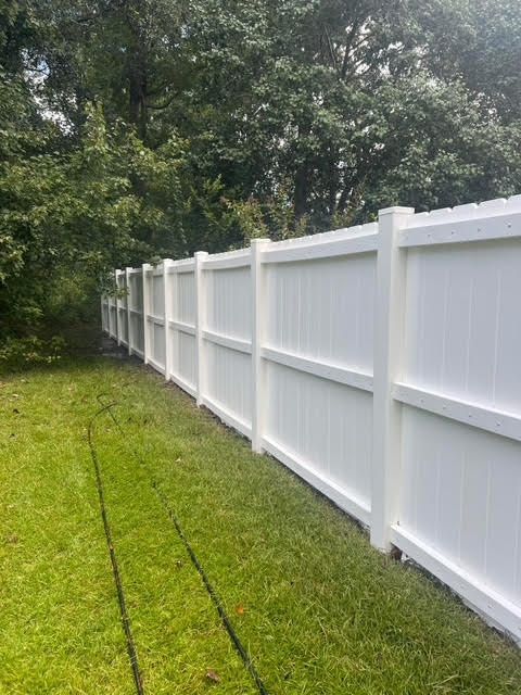 White vinyl fence in a grassy yard, trees in the background.