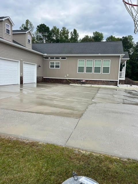 A house with three garage doors and a basketball hoop. The driveway is wet, and the sky is overcast.