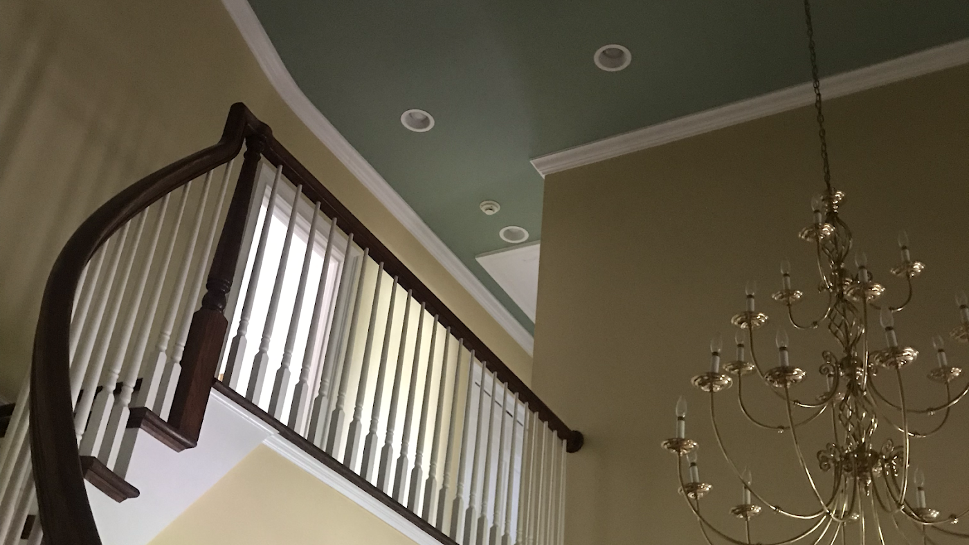 A two-story entryway with a curved staircase, chandelier, and pale green ceiling.
