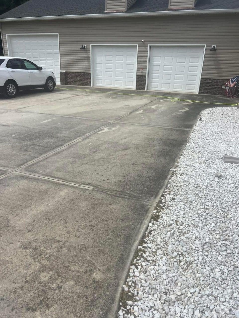 Driveway leading to a three-car garage. Driveway is stained. A white SUV is parked near the first garage door.