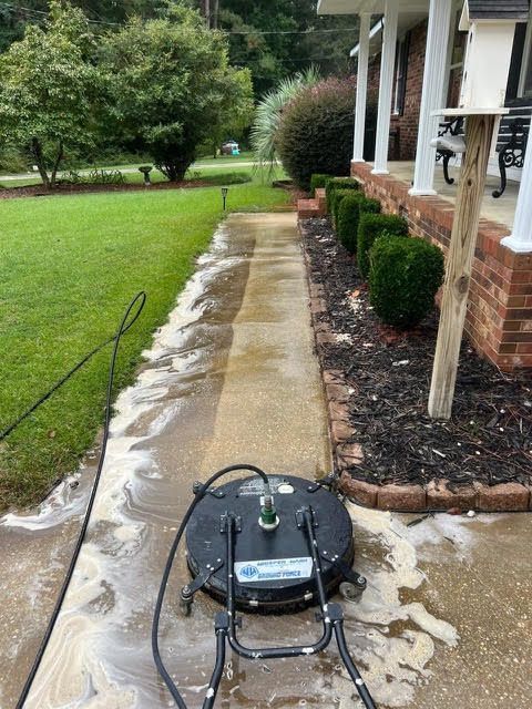 A person power washing a concrete walkway. Black machine on concrete, surrounded by soap and water.