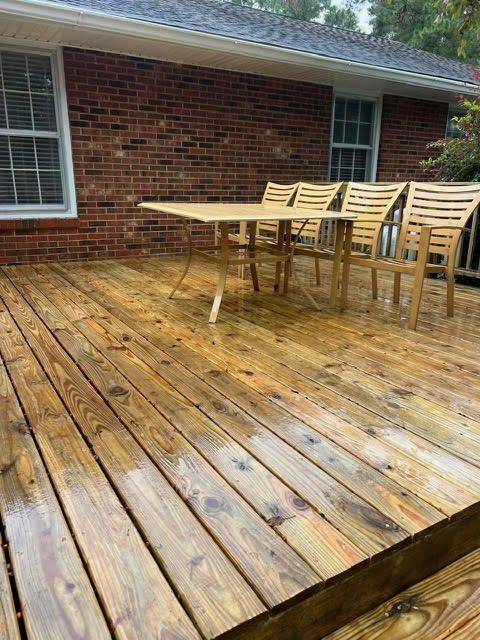 Wooden deck with table and chairs against a brick building with windows.