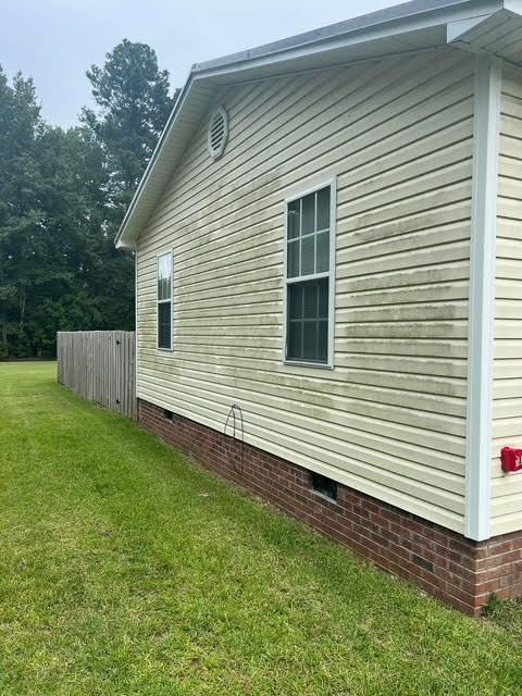 Yellow siding on a house shows mildew and dirt, next to a green lawn and wooden fence.