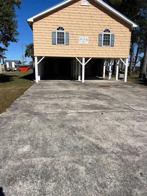 Tan stilt house with two windows and a concrete driveway.