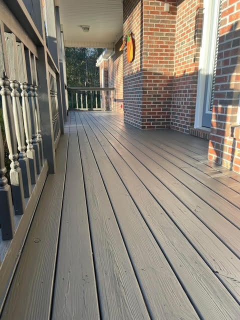 A shaded porch with gray composite decking, brick wall, and ornate railing.