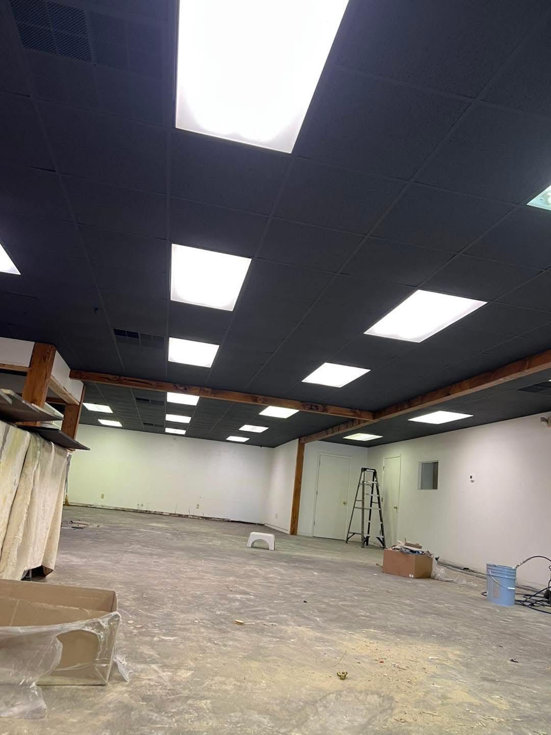 Empty room under construction with black ceiling, white walls, and bright square lights.