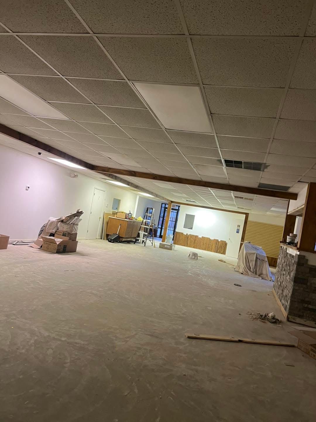 An unfinished room under construction, with exposed ceiling tiles, beams, and construction materials.