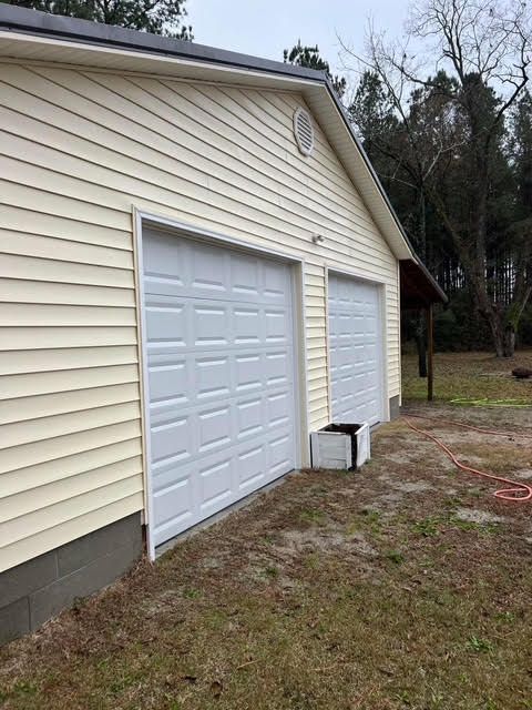 Two-car garage with white doors, yellow siding, and concrete foundation. Grass and trees in the background.