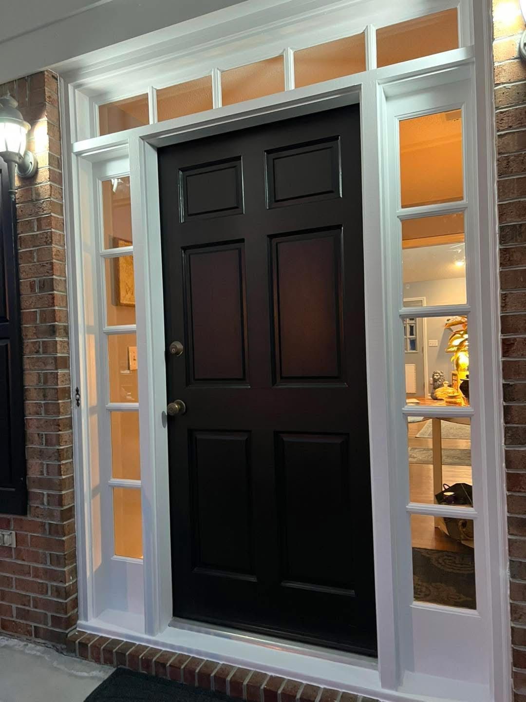 Black front door with white trim, sidelights, and overhead transom windows. Red brick exterior.