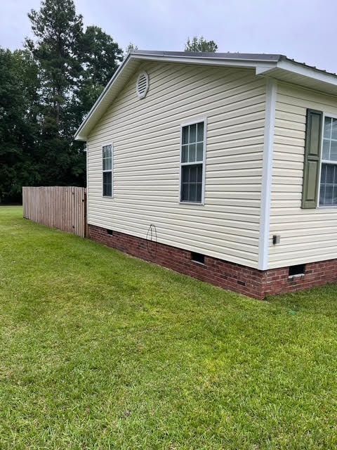 Beige house with green shutters and red brick base. A wooden fence and green lawn are in the foreground.