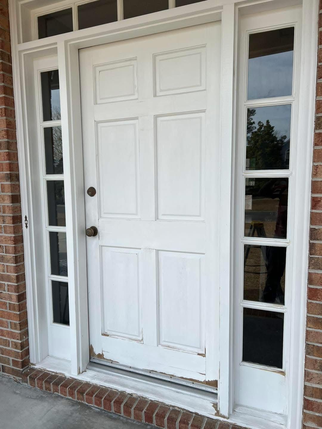 White front door with sidelights, weathered paint, brick exterior.
