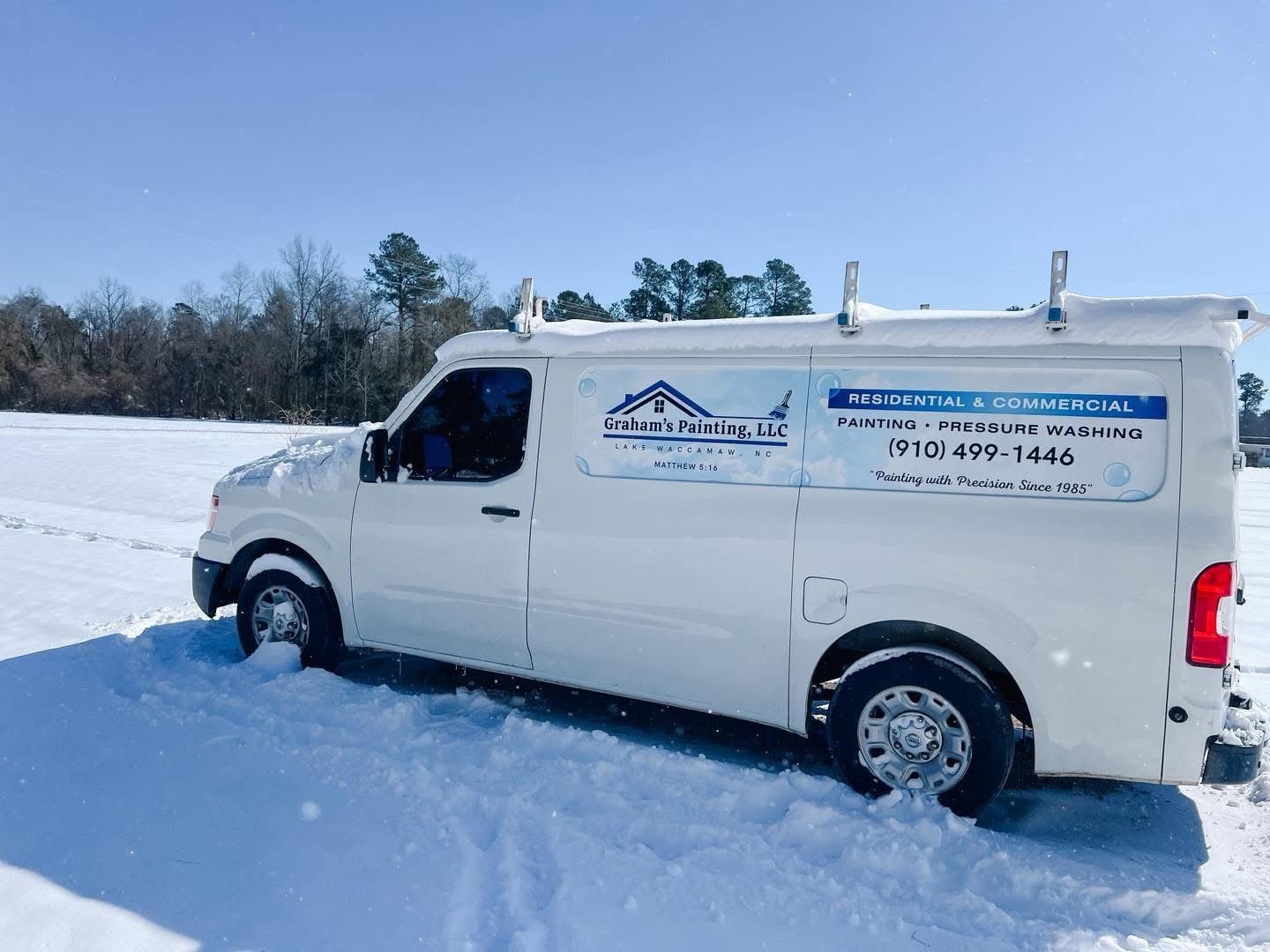 White van with company logo stuck in snow-covered field on a sunny day.