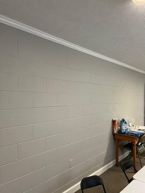 Gray painted cinder block wall with white crown molding. A table with supplies sits near the corner.