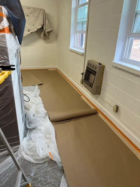 Room with brown paper floor covering, small windows, and a wall heater.