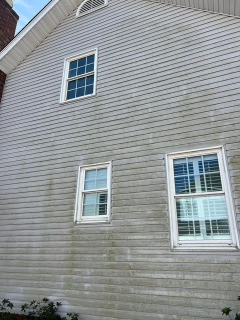 Gray weathered clapboard siding on a house with three white-framed windows.