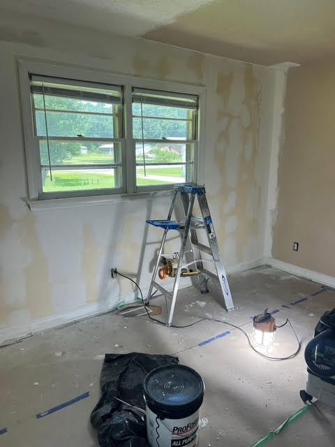 Room under renovation; ladder, window, paint cans, and work light present. Walls show patchy paint.