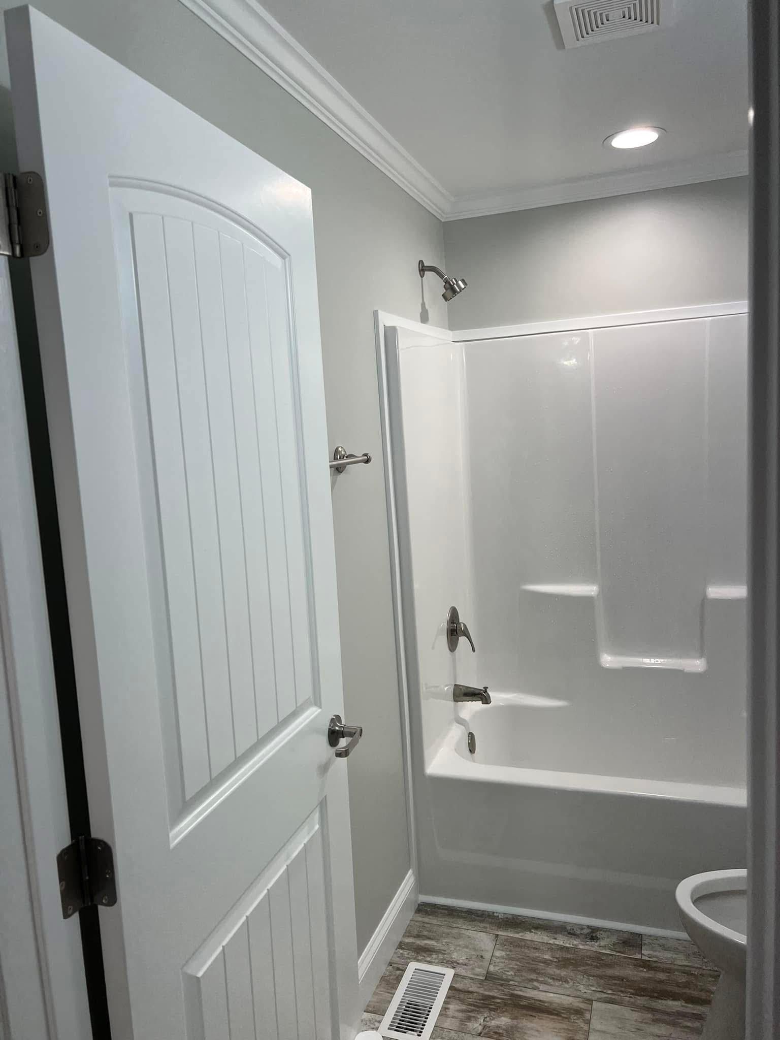 Bathroom with white tub/shower, door, and fixtures, gray walls, and patterned flooring.