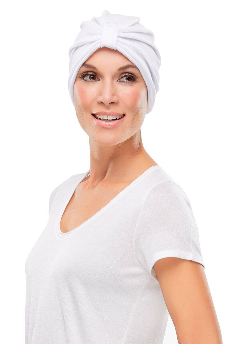 A woman wearing a white turban and a white shirt is smiling.