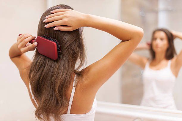 A woman is brushing her hair in front of a mirror.