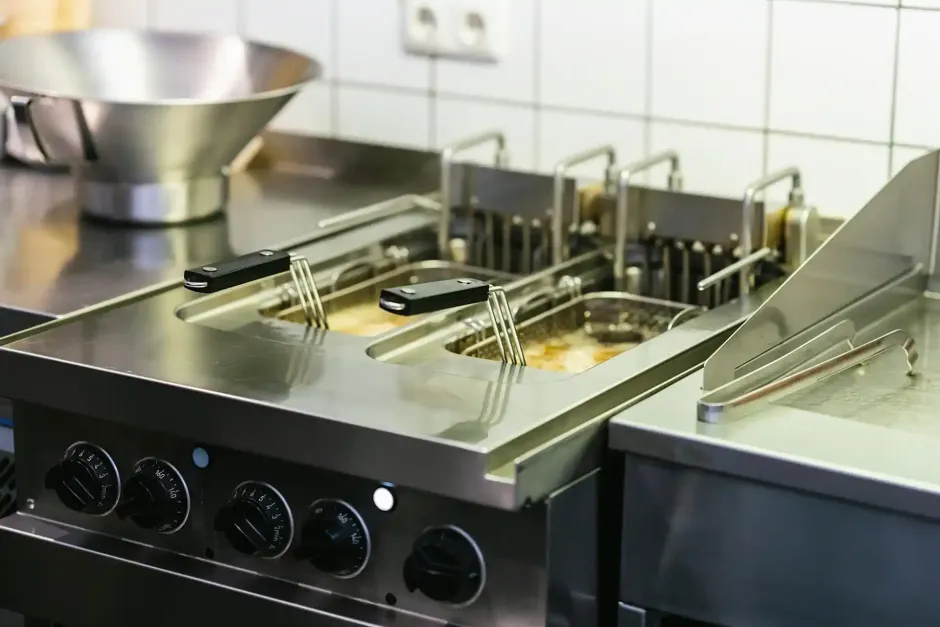 Friggitrice professionale in acciaio inox in una cucina con cestelli e vaschette per l'olio in metallo.