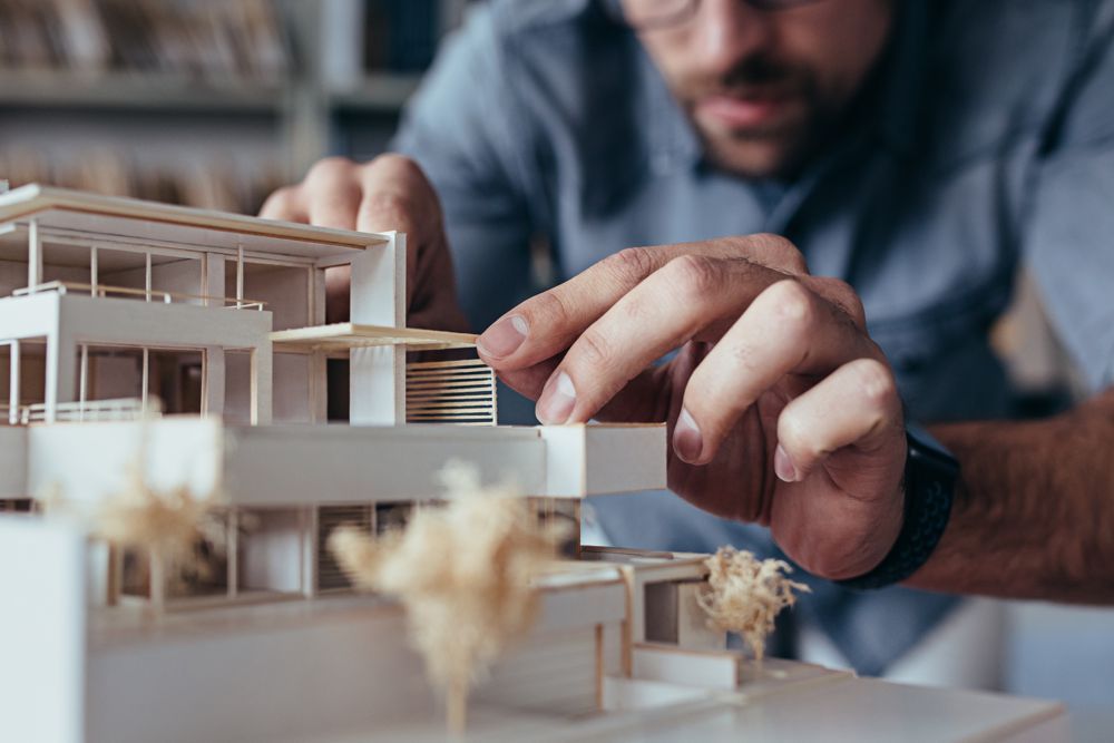 A person carefully adjusting a detailed white architectural model of a modern house.