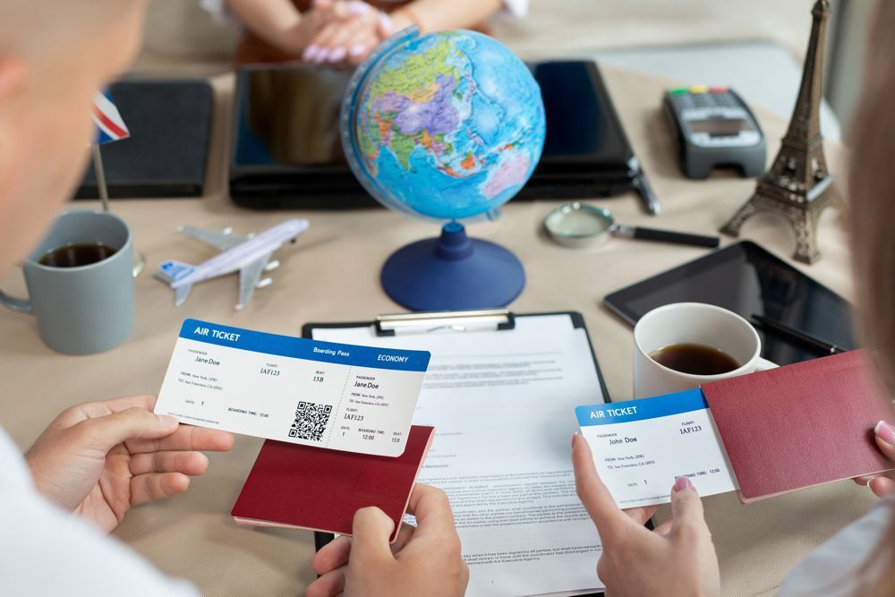Two people holding passports and plane tickets over a table with a globe, documents, and travel-themed items.