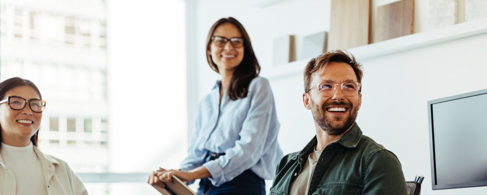Three colleagues in a bright, modern office space are smiling and engaged in a collaborative discussion.