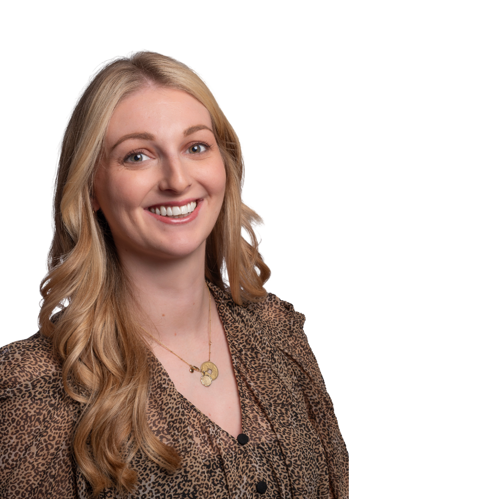 Smiling person with long blonde hair wearing a patterned, brown, button-down shirt and a small gold pendant necklace.
