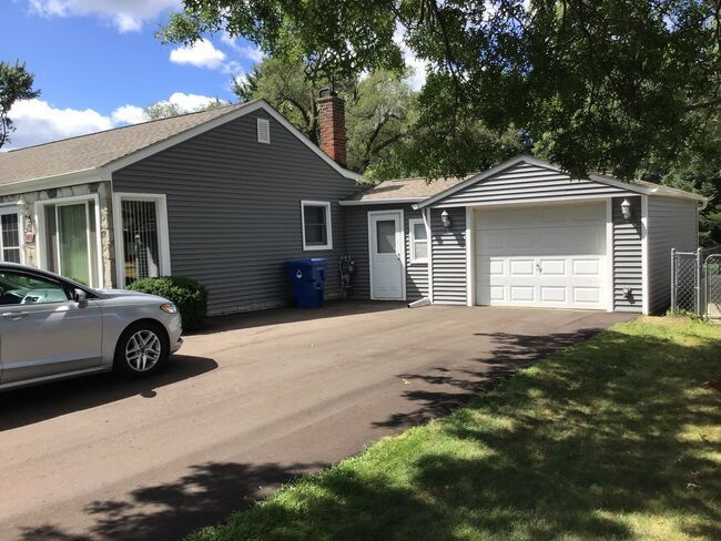 Suburban house with attached garage, driveway, parked car, and trees casting shade.