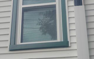 Close-up of a white house window with teal trim and closed blinds.