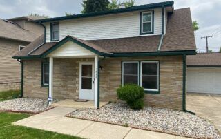 Brick two-story house with white trim, front porch, and gravel landscaping in a suburban neighborhood