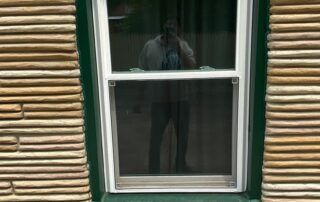 Person reflected in a window with white trim on a green building and tan siding