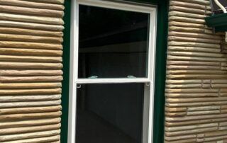 A white-framed window on a log cabin wall with horizontal wooden logs.