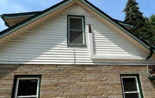 House exterior with white siding, tan stone facade, and two windows under a peaked roof