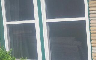 Two white-trimmed windows with dark curtains on a house exterior
