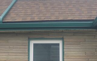 House roof and upper wall with white-trimmed window and brown shingles