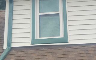 House exterior with white siding, teal-trimmed window, and brown shingled roofline