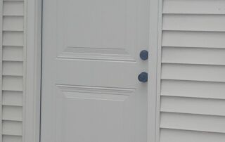 White front door with two blue doorknobs and light gray siding around it