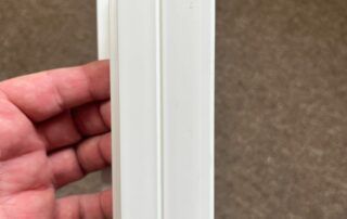 Hand holding a white vertical plastic trim or molding strip against a brown carpeted background