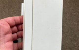 Hand holding a white rectangular panel against a brown carpet background